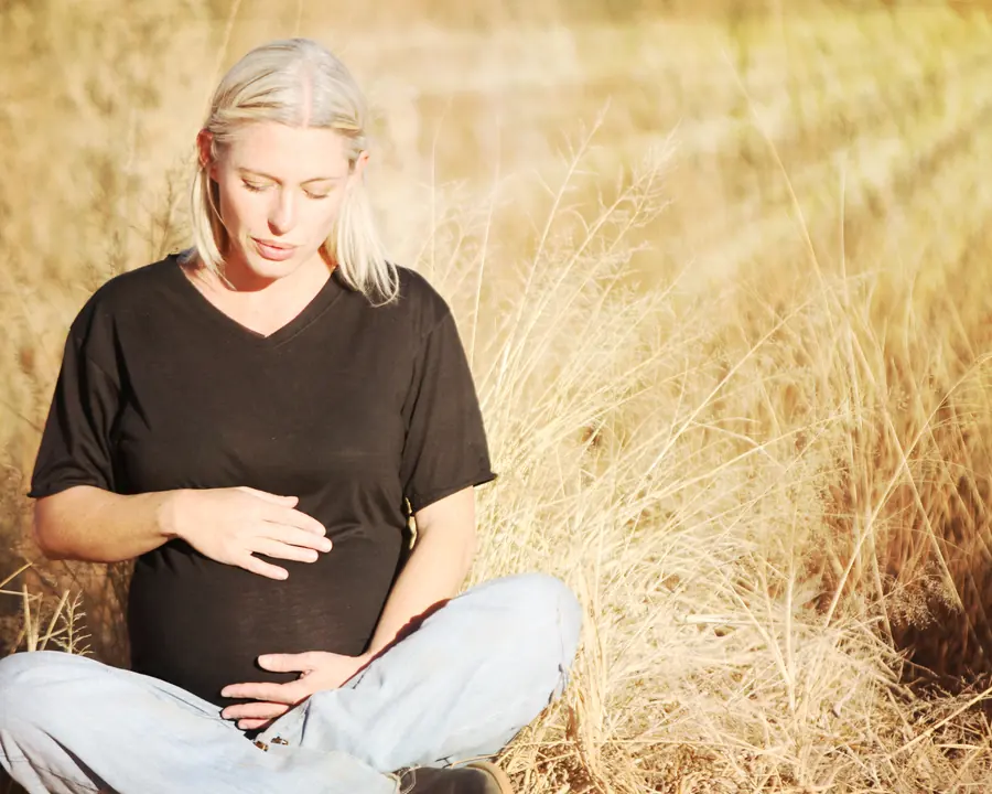 Pregnant woman sitting cross-legged in tall golden grass