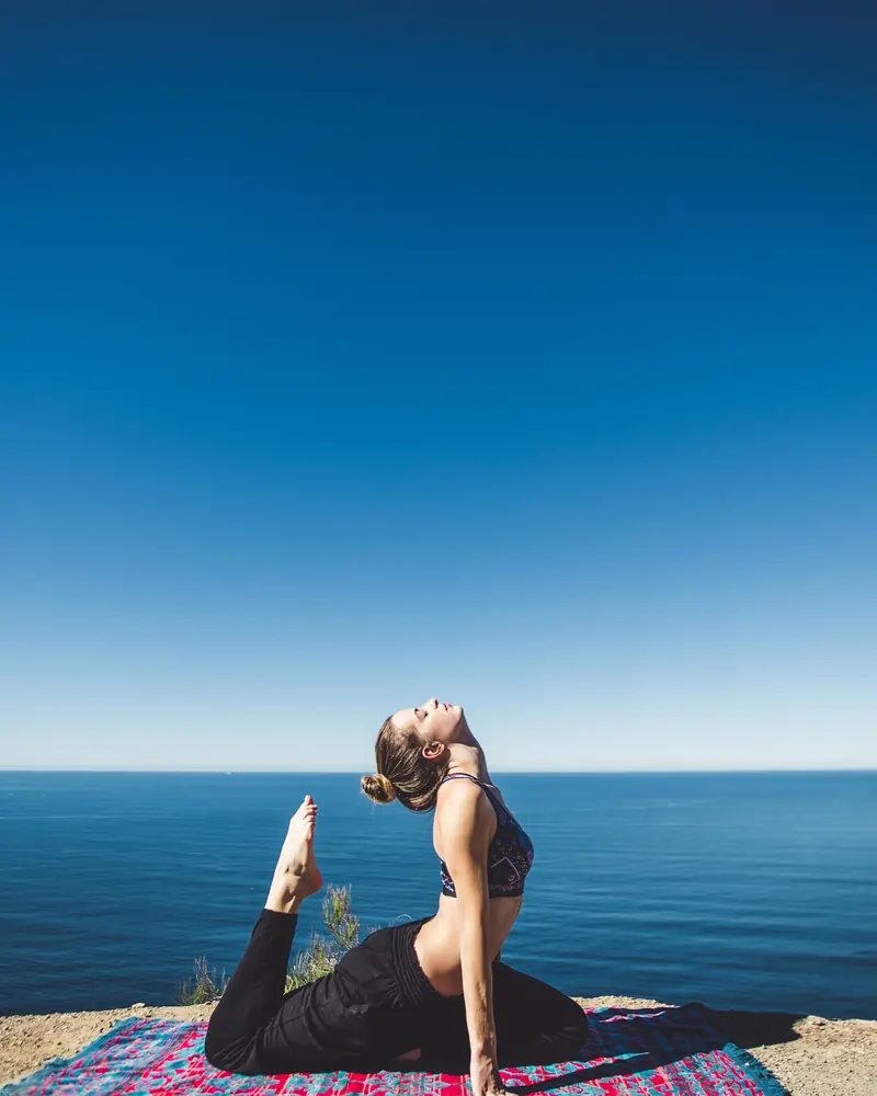 Woman in a seated backbend on a mat at the edge of a sea cliff